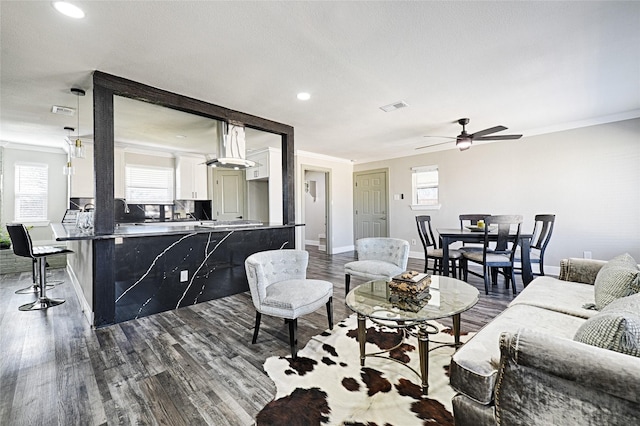 living area featuring a wealth of natural light, ornamental molding, dark wood finished floors, and visible vents