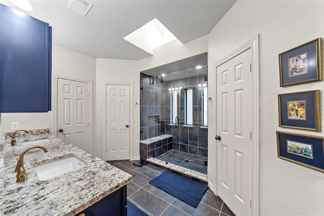 bathroom featuring tile patterned floors, vanity, a tile shower, and a skylight