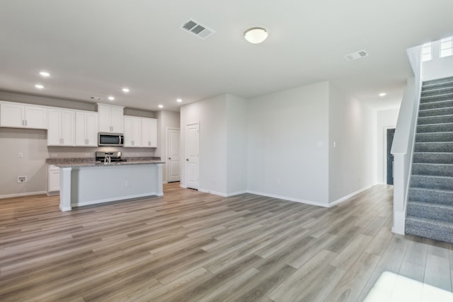 kitchen featuring white cabinetry, a center island with sink, light wood-type flooring, and stainless steel appliances