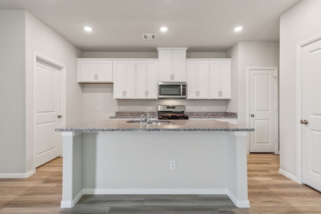 kitchen featuring stainless steel appliances, white cabinets, light stone counters, and a kitchen island with sink