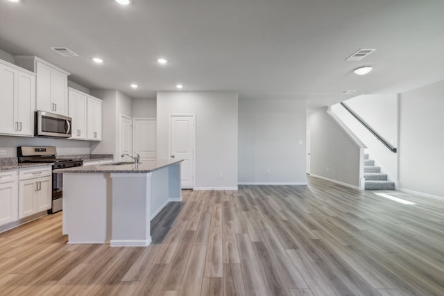 kitchen featuring white cabinetry, stainless steel appliances, sink, stone countertops, and a center island with sink