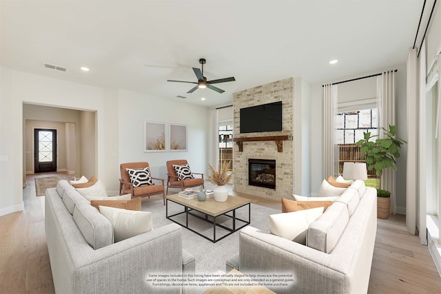 living room featuring a fireplace, a wealth of natural light, ceiling fan, and light hardwood / wood-style flooring