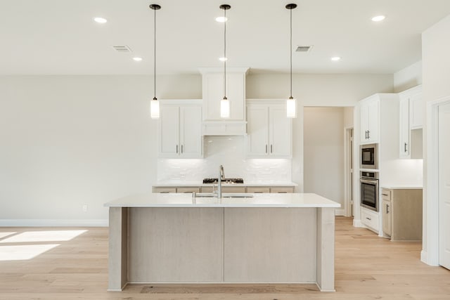 kitchen with black microwave, white cabinets, a kitchen island with sink, light wood-type flooring, and stainless steel oven