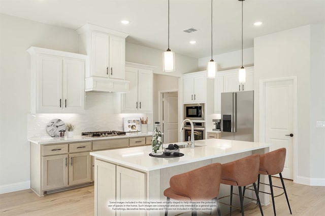 kitchen with stainless steel appliances, light wood-type flooring, exhaust hood, an island with sink, and white cabinets