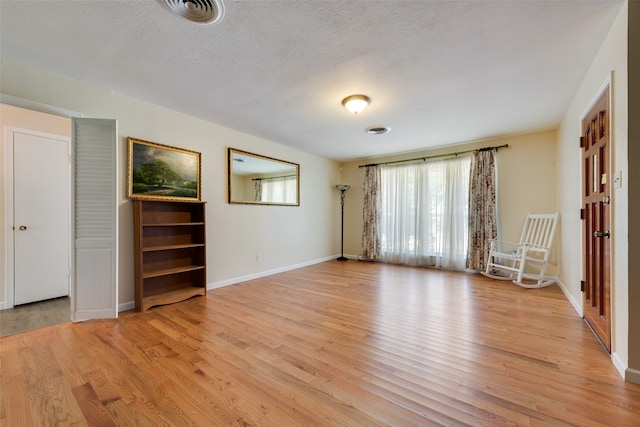 unfurnished room with light wood-type flooring and a textured ceiling