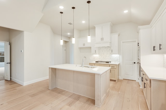 kitchen featuring stainless steel gas cooktop, a center island with sink, white cabinets, and light wood-type flooring