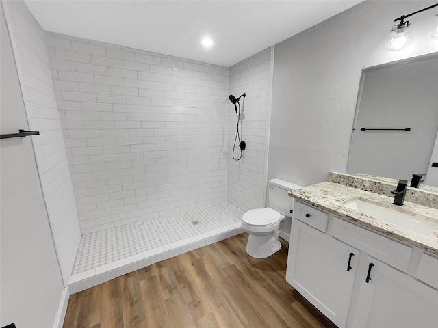 bathroom with tiled shower, hardwood / wood-style floors, vanity, and toilet