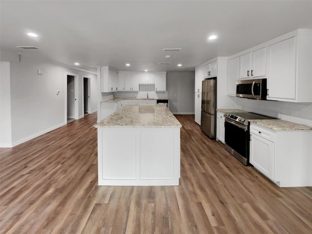 kitchen with white cabinets, light hardwood / wood-style floors, light stone countertops, and appliances with stainless steel finishes