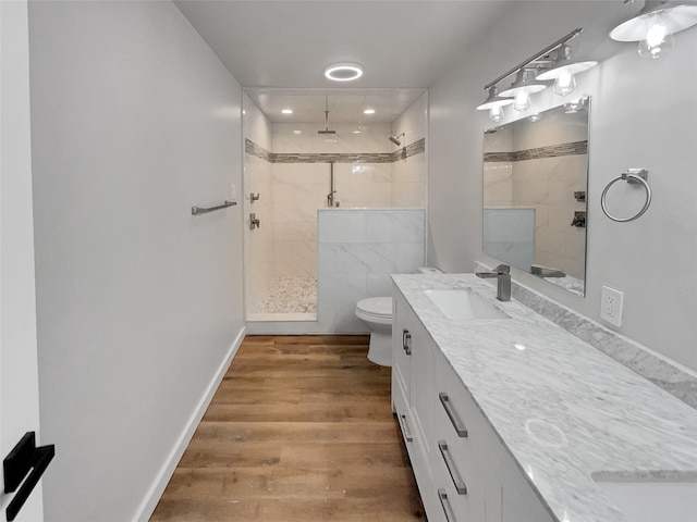 bathroom with a tile shower, vanity, toilet, and wood-type flooring