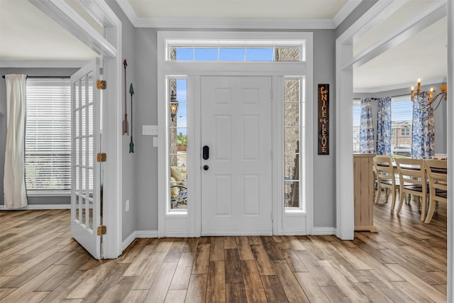 entrance foyer featuring light hardwood / wood-style flooring, ornamental molding, and a notable chandelier