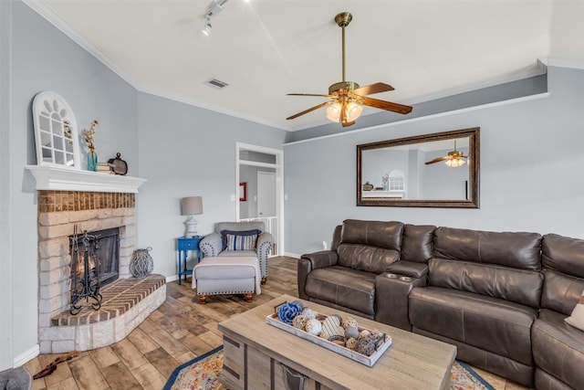 living room featuring a stone fireplace, rail lighting, hardwood / wood-style flooring, ceiling fan, and ornamental molding