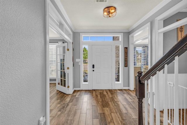 foyer entrance featuring wood finished floors, a textured wall, ornamental molding, and visible vents