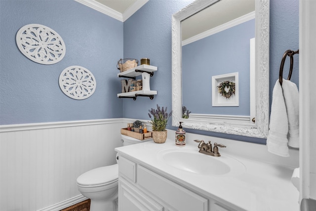 half bathroom featuring ornamental molding, toilet, a textured wall, vanity, and a wainscoted wall