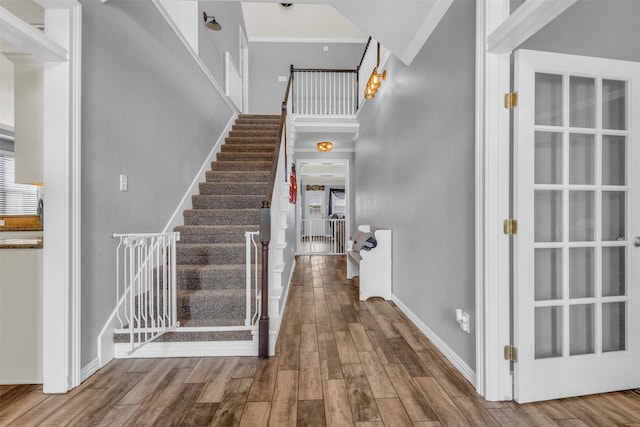 staircase featuring wood finished floors, baseboards, ornamental molding, and a towering ceiling