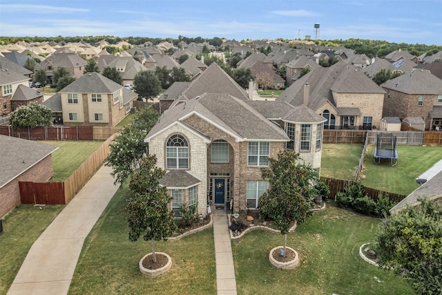traditional-style home with a trampoline, a residential view, a front lawn, brick siding, and a fenced backyard