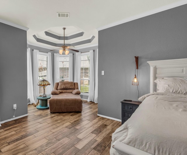 bedroom featuring hardwood / wood-style floors, ceiling fan, ornamental molding, and a tray ceiling