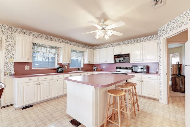 kitchen featuring range with electric stovetop, a kitchen island, a breakfast bar, white cabinetry, and ceiling fan