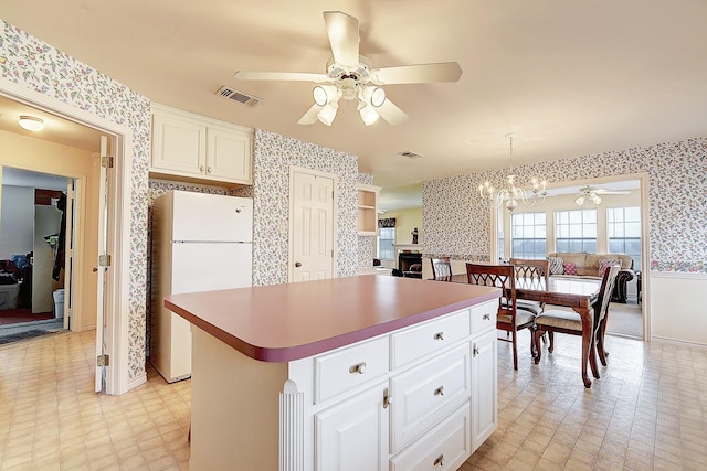 kitchen featuring a kitchen island, ceiling fan with notable chandelier, decorative light fixtures, white cabinets, and white fridge