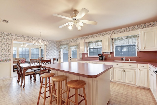 kitchen featuring sink, hanging light fixtures, a healthy amount of sunlight, a kitchen island, and ceiling fan with notable chandelier