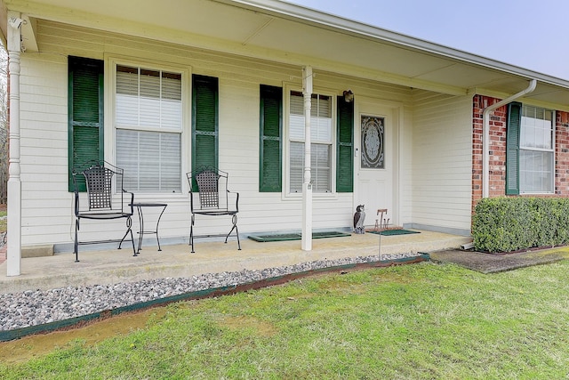 view of exterior entry with a lawn and a porch