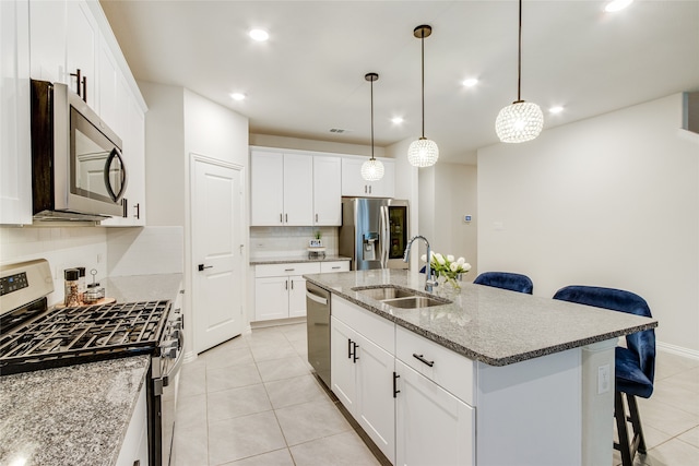 kitchen with a breakfast bar, backsplash, stainless steel appliances, pendant lighting, and a center island with sink