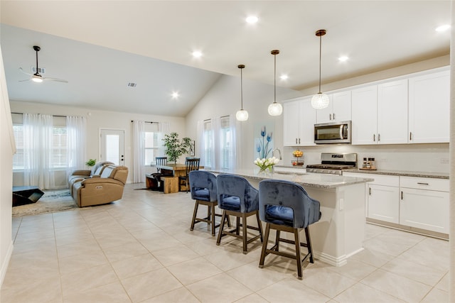 kitchen with appliances with stainless steel finishes, a center island with sink, pendant lighting, light stone counters, and white cabinetry