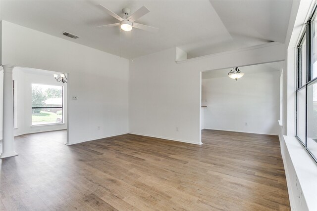 spare room with hardwood / wood-style flooring, ceiling fan with notable chandelier, decorative columns, and lofted ceiling