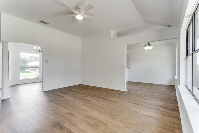 empty room with ceiling fan with notable chandelier, visible vents, baseboards, light wood-type flooring, and decorative columns