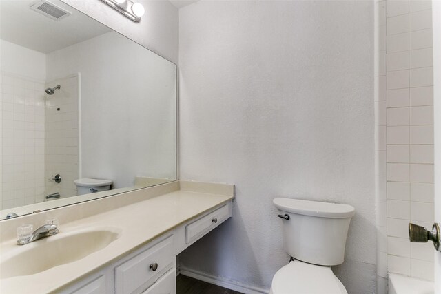 bathroom with a tile shower, vanity, and toilet