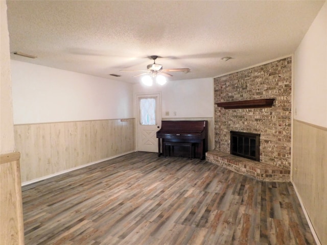 unfurnished living room with hardwood / wood-style flooring, a textured ceiling, a brick fireplace, brick wall, and ceiling fan