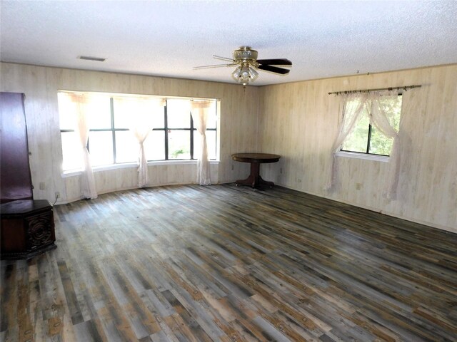 unfurnished living room featuring a wood stove, a textured ceiling, ceiling fan, and dark hardwood / wood-style floors