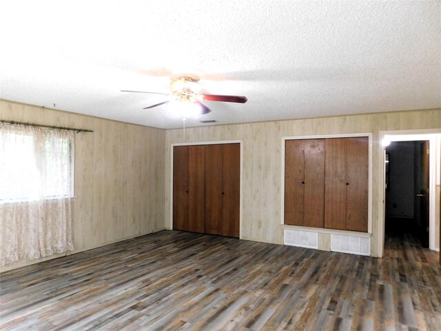 unfurnished bedroom featuring two closets, ceiling fan, a textured ceiling, and dark hardwood / wood-style flooring