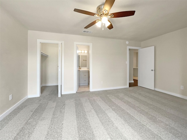 unfurnished bedroom with ensuite bath, a closet, light colored carpet, a walk in closet, and ceiling fan