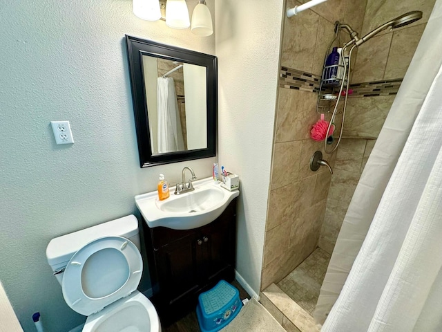 bathroom with toilet, tiled shower, vanity, and a textured wall