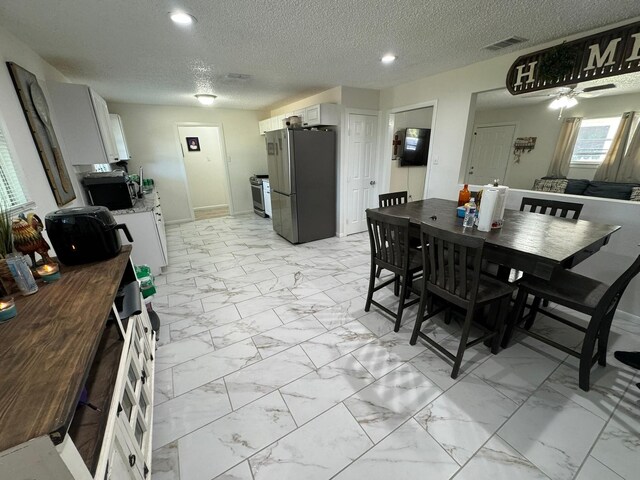 kitchen featuring stainless steel fridge, light tile patterned flooring, ceiling fan, and white cabinetry