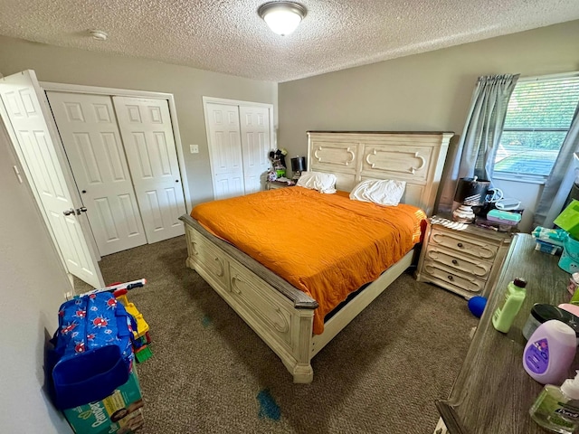bedroom with a textured ceiling, two closets, and dark colored carpet