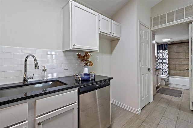 kitchen with sink, stainless steel dishwasher, backsplash, dark stone counters, and white cabinets