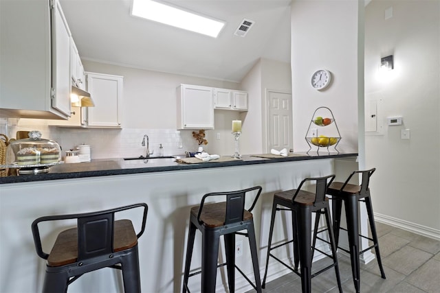 kitchen featuring sink, kitchen peninsula, a kitchen bar, decorative backsplash, and white cabinets