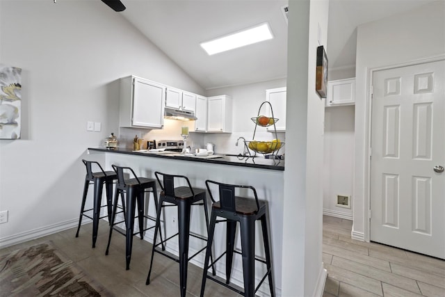 kitchen featuring backsplash, kitchen peninsula, vaulted ceiling, white cabinetry, and a breakfast bar area