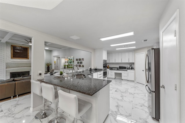 kitchen with kitchen peninsula, stainless steel appliances, a kitchen bar, white cabinetry, and dark stone counters