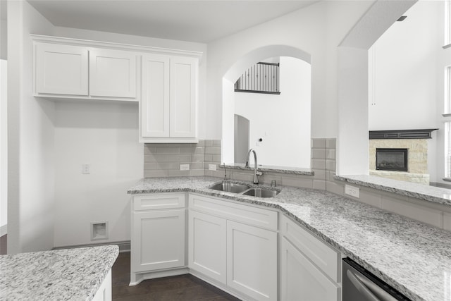 kitchen featuring a stone fireplace, sink, decorative backsplash, and white cabinetry