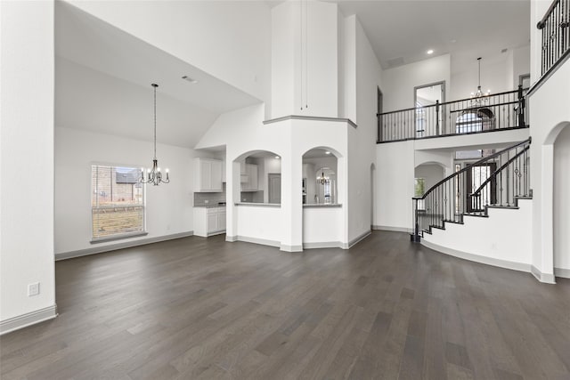 unfurnished living room featuring dark wood-type flooring, a towering ceiling, and a notable chandelier