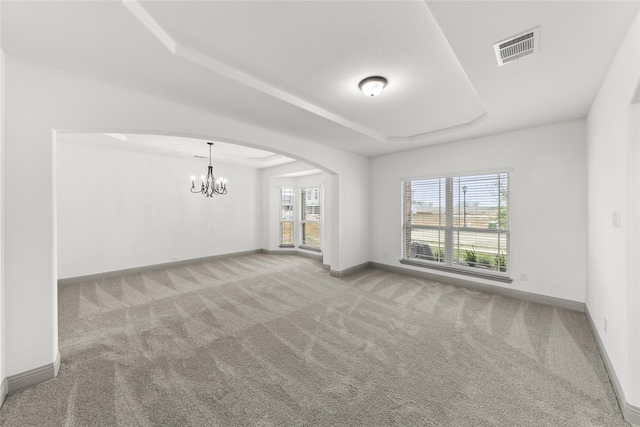 empty room featuring a raised ceiling, plenty of natural light, carpet floors, and an inviting chandelier