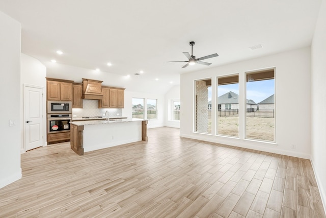 kitchen featuring sink, a center island with sink, decorative backsplash, and light stone countertops