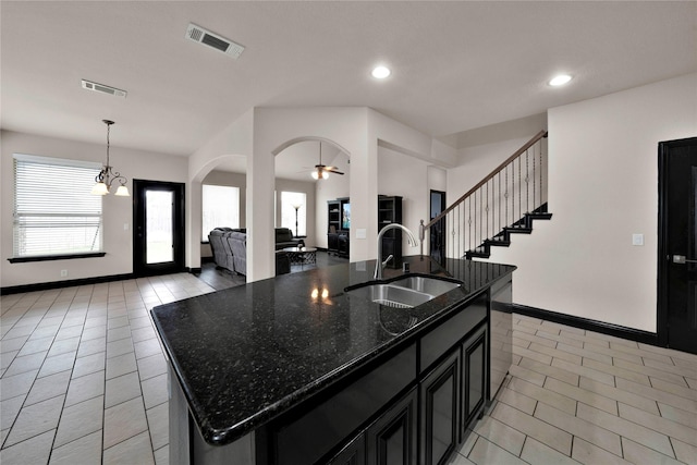 kitchen with sink, dark stone countertops, decorative light fixtures, a kitchen island with sink, and ceiling fan with notable chandelier