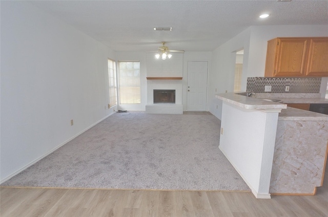 kitchen with decorative backsplash, ceiling fan, kitchen peninsula, light carpet, and a textured ceiling