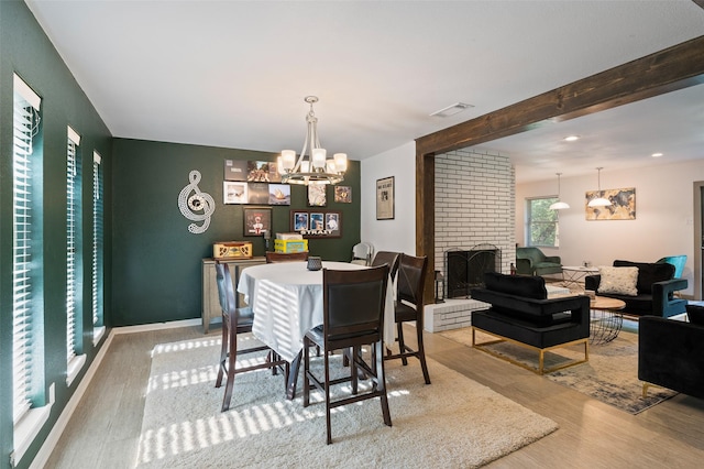 dining space featuring a fireplace, a chandelier, beamed ceiling, and light wood-type flooring