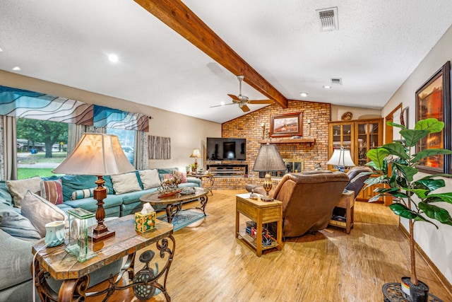 living room with a brick fireplace, lofted ceiling with beams, brick wall, a textured ceiling, and light wood-type flooring