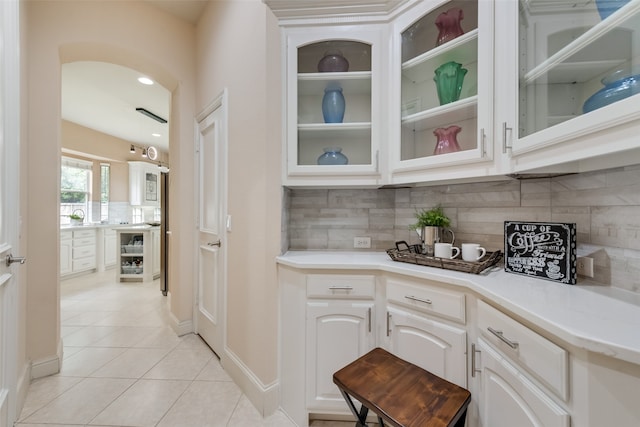 bar with tasteful backsplash, white cabinetry, and light tile patterned flooring