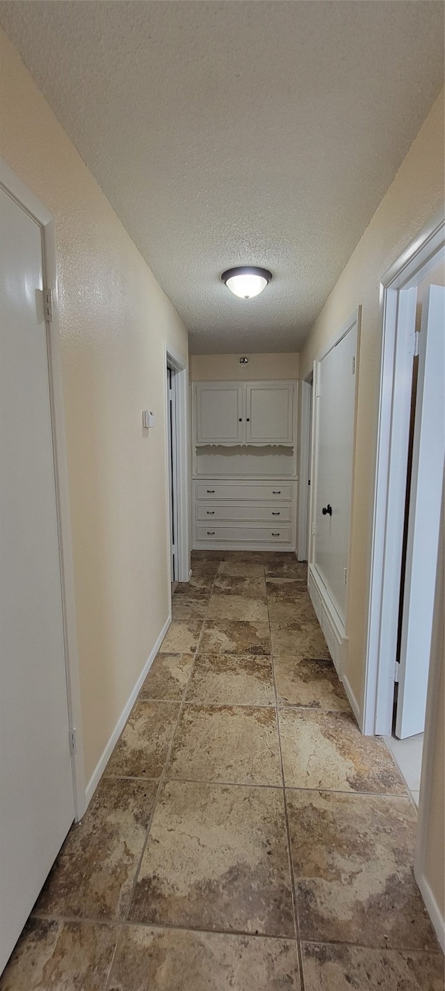 hallway with a textured ceiling and light tile patterned floors